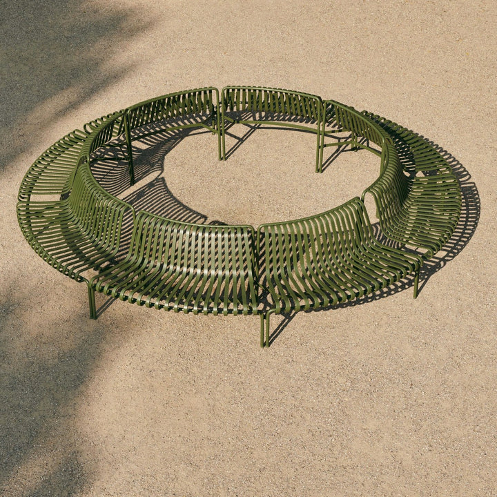 An olive green circular outdoor bench with a slatted metal design, shown from an elevated angle on a sandy ground.