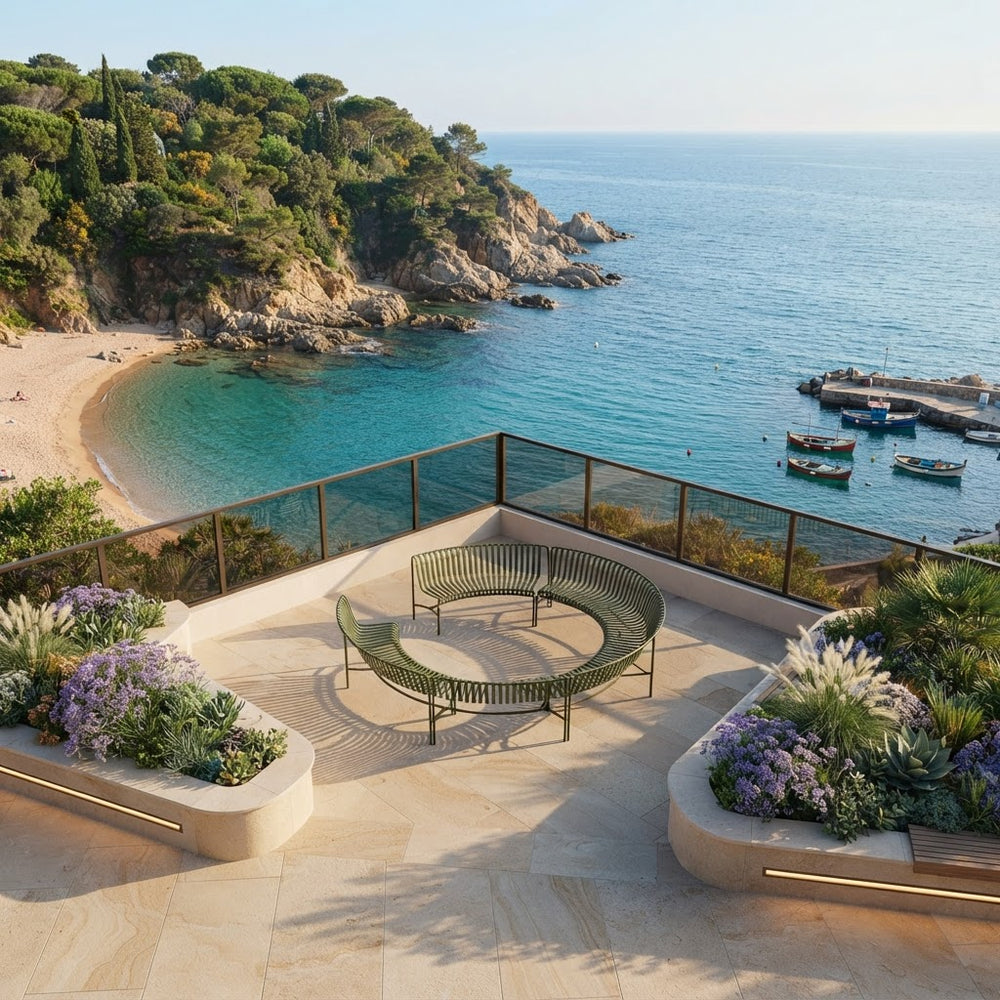Modern outdoor curved bench on a stone terrace overlooking a turquoise bay, rocky coastline, sandy beach, and small boats.