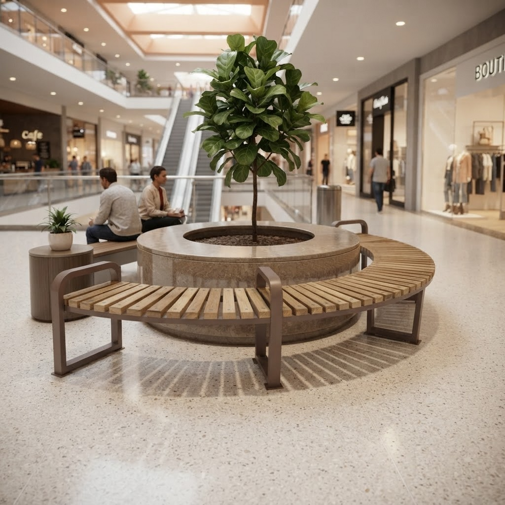 A modern curved wooden slat bench with dark metal arms arranged around a round concrete planter holding a leafy tree, set in a bright, spacious indoor shopping mall.