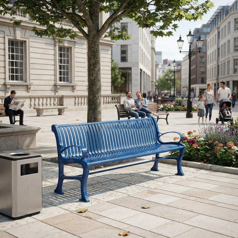 A bright blue metal park bench in a city plaza, shown in a real outdoor environment with people sitting and walking nearby, trees, buildings, and a trash can in the foreground.