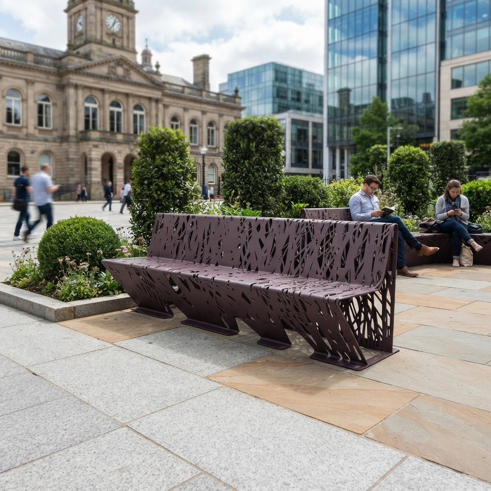 A modern sculptural metal bench with a laser-cut lattice pattern sits in a public plaza. Two people are seated on the bench, and a historic stone building and glass skyscrapers are visible in the background.