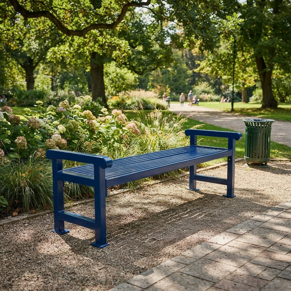 A blue wooden park bench with armrests, situated on a paved path in a lush green park with trees and flowers.