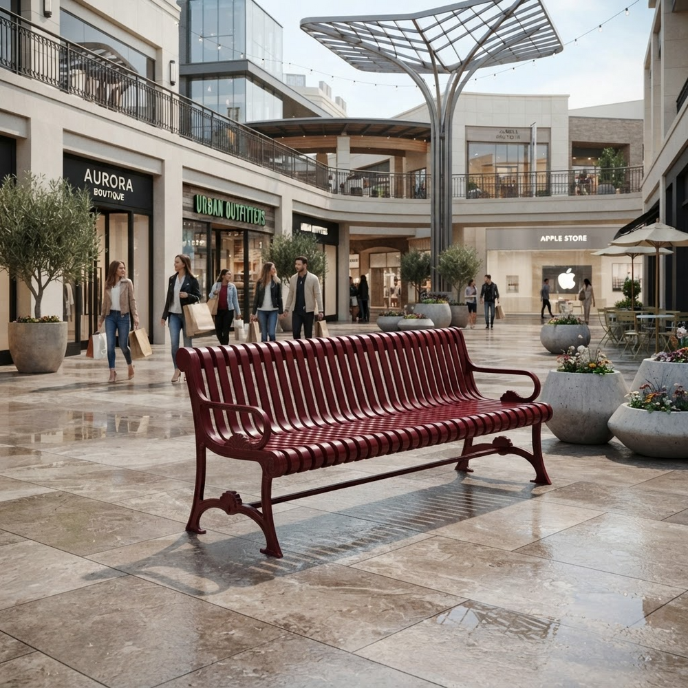 A red slatted outdoor bench sits in a modern shopping mall atrium with stone tile floors, potted trees, and shoppers walking in the background.