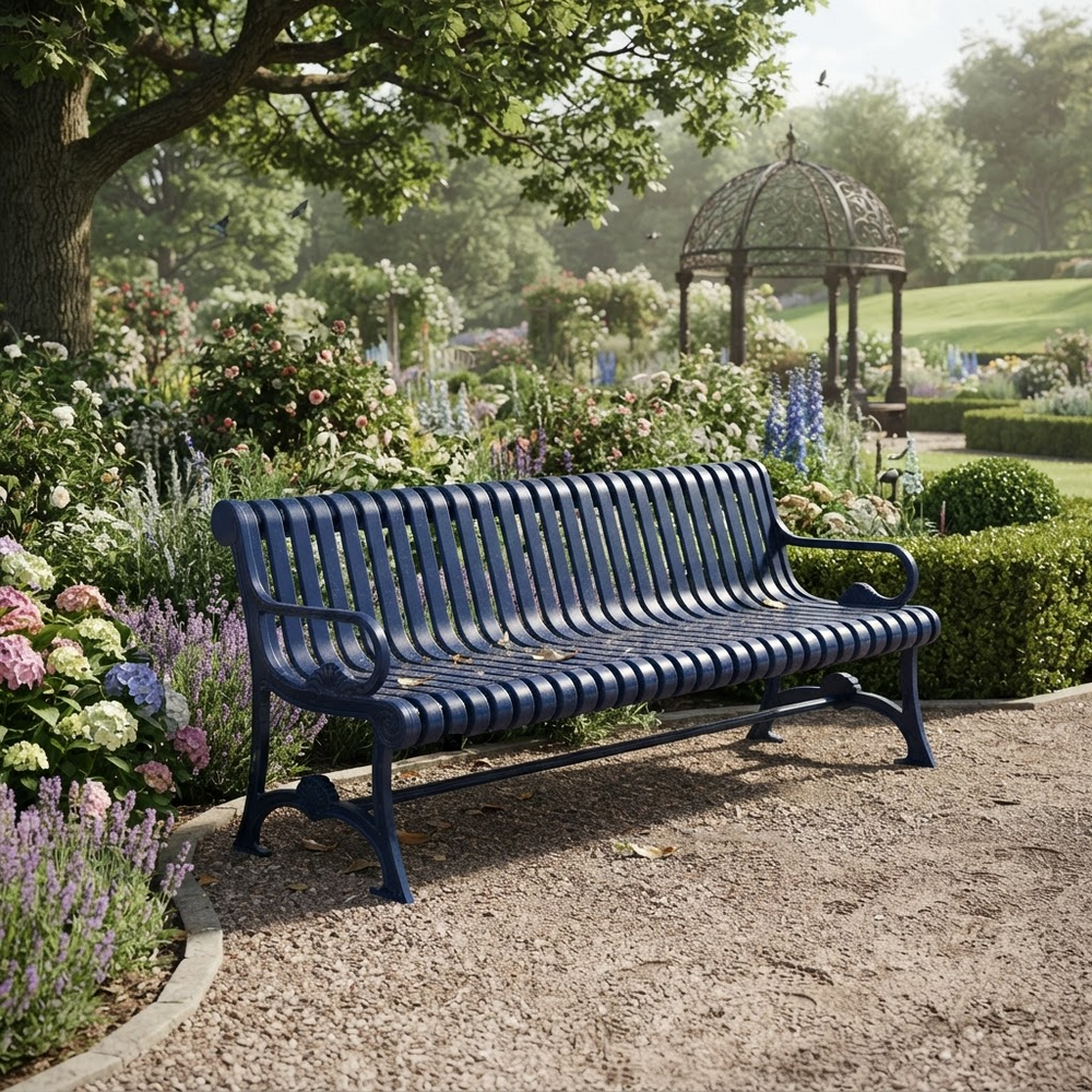 A dark blue metal garden bench with a slatted back and seat, positioned on a gravel path in a lush, sunlit garden with flowers, a tree, and a gazebo in the background.