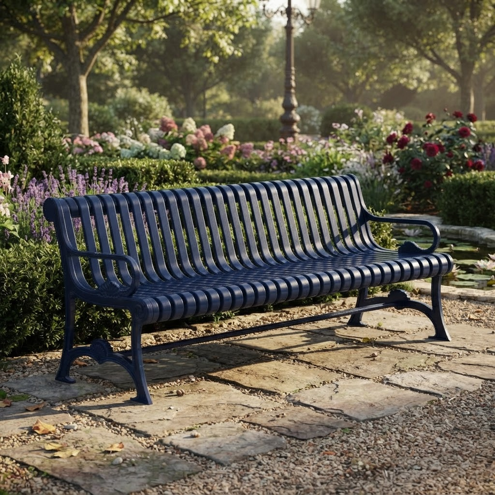 A dark navy blue metal park bench with a slatted back and seat, positioned on a stone pathway in a lush, sunlit garden with flowers and trees in the background.