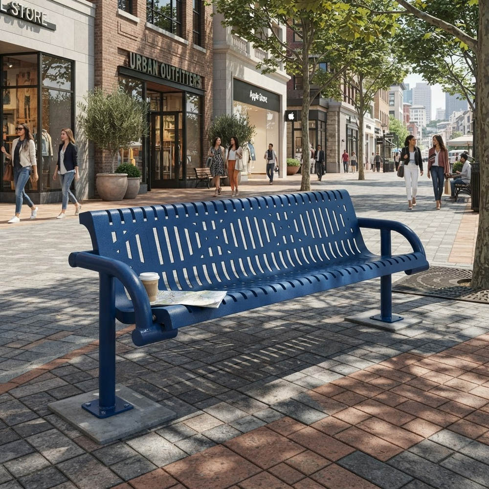 A blue metal urban bench with a slatted back and seat, mounted on a square concrete base, placed on a paved city sidewalk. The bench has armrests and a small cup holder on the left side.