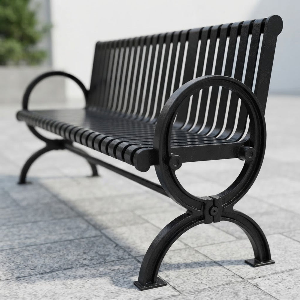A black metal park bench with a slatted back and seat, shown outdoors on a light gray paved surface with a blurred background.