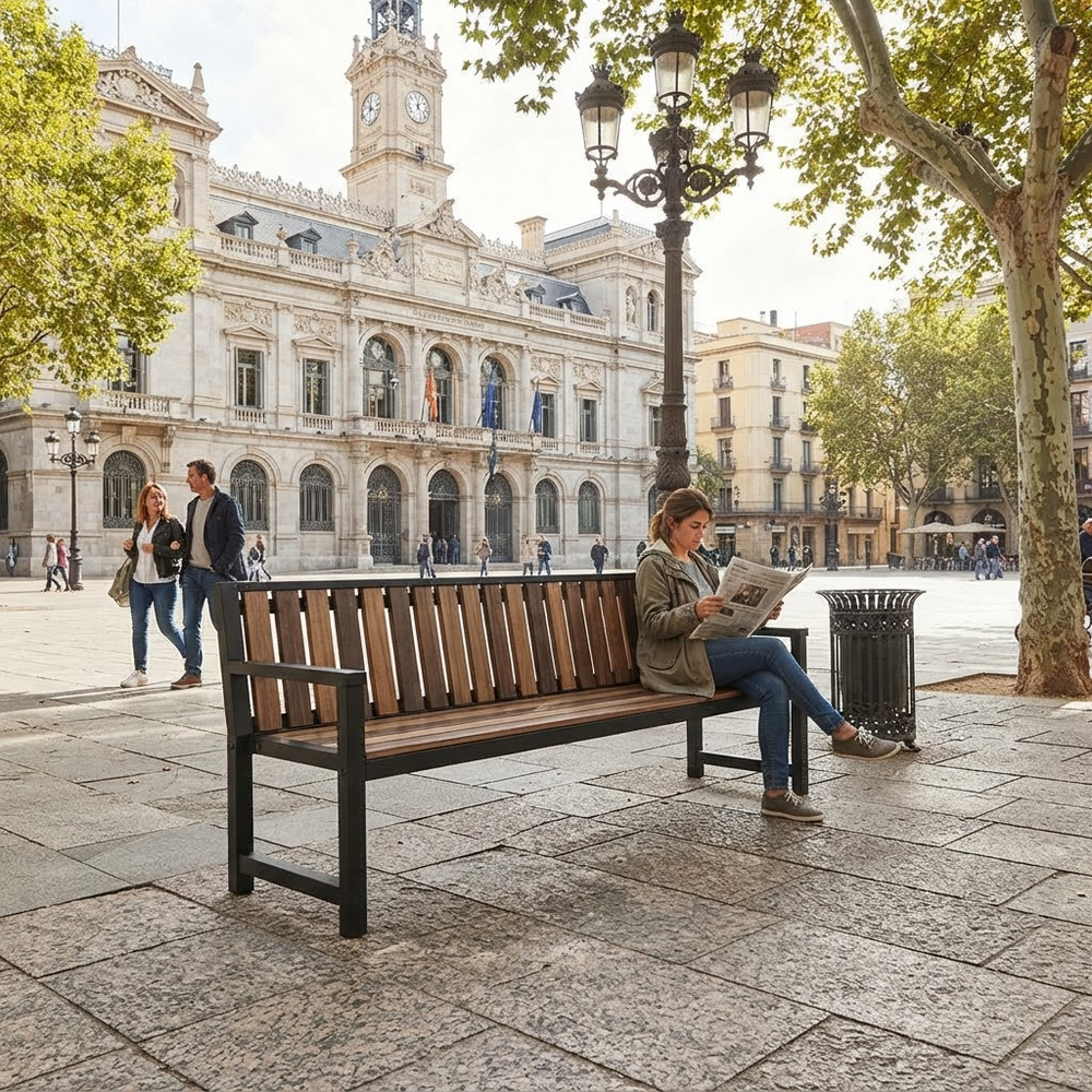 A wooden slat bench with a black metal frame sits in a public square, with a woman sitting on it and reading a newspaper. A large historic building, trees, and street lamps are visible in the background.
