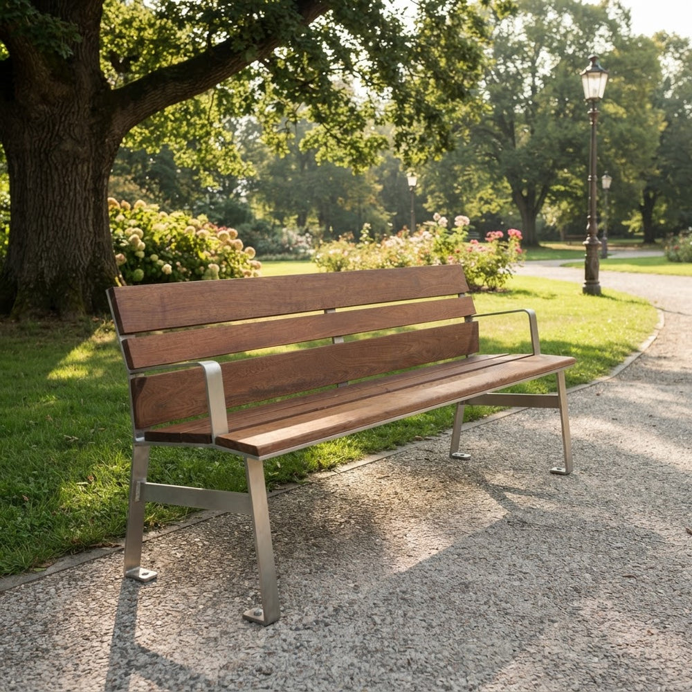 A modern wooden park bench with a brown wood-grain slatted back and seat, supported by a silver metal frame, situated on a gravel path in a sunny park with green grass and trees.