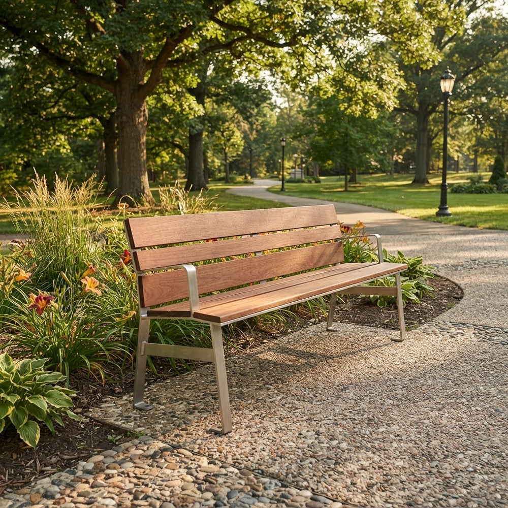 A wooden park bench with a weathered brown finish and silver metal legs, situated on a gravel path in a lush green park.