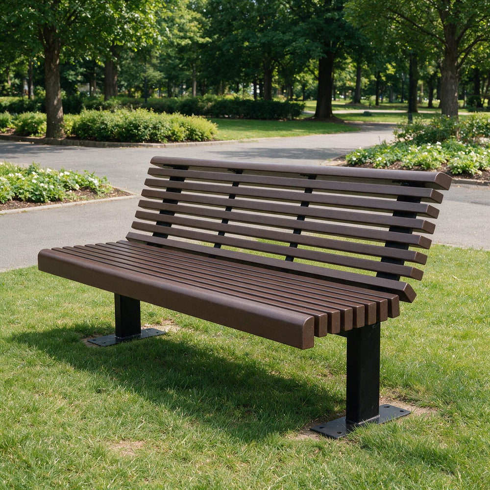 A modern slatted park bench made of dark brown composite material with black metal legs, situated on a green grassy lawn in a park with trees and a paved path in the background.