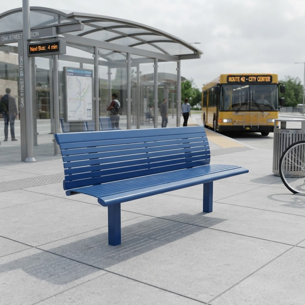 A blue slatted outdoor bench sits on a paved transit station platform, with a yellow bus, station shelter, and a few people visible in the background.