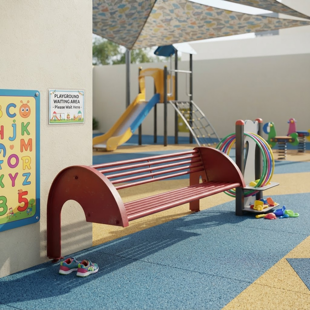 A red curved park bench sits on a blue and yellow playground surface next to a playground sign and a play structure, with a canopy overhead and a play area in the background.