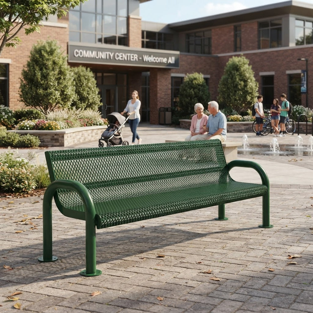 A green metal mesh bench in an outdoor paved plaza in front of a brick community center building, with people sitting and walking in the background.