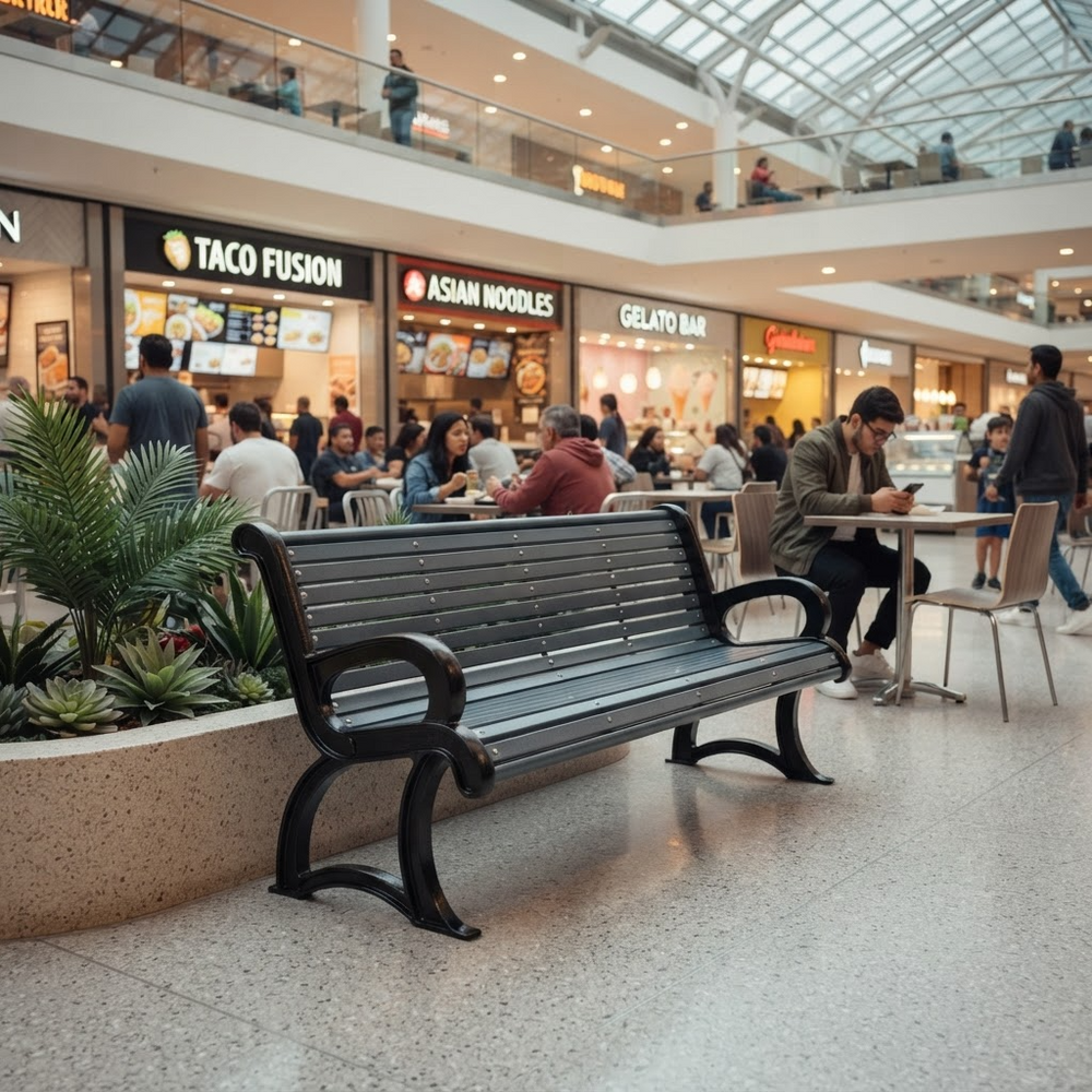 A black slatted public bench sits in the foreground of a busy multi-level shopping mall food court, with people seated at tables and storefronts including Taco Fusion and Asian Noodles in the background.