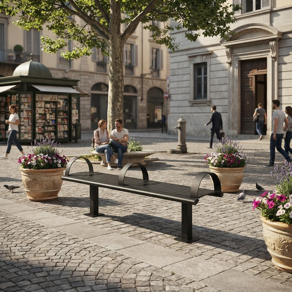A black metal park bench in a cobblestone plaza with people sitting nearby, potted flowers, trees, and historic buildings in the background.