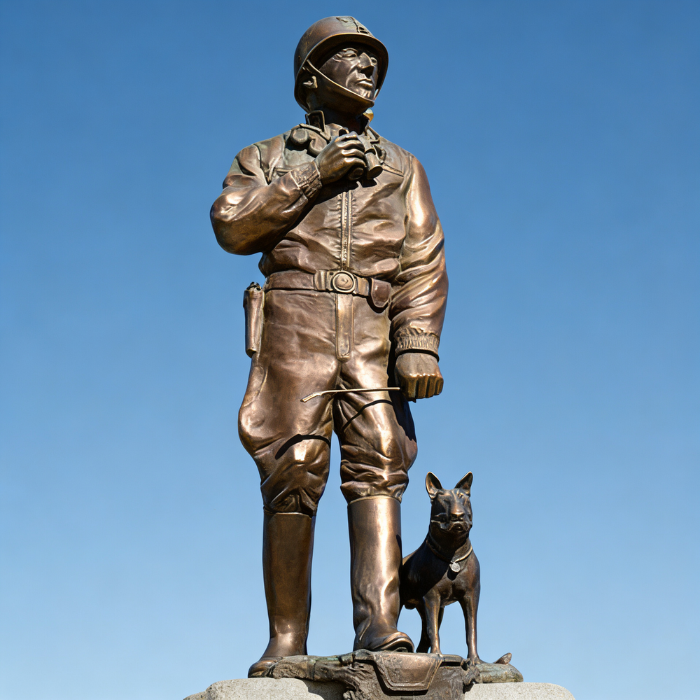 Bronze statue of a soldier with a dog against a clear blue sky