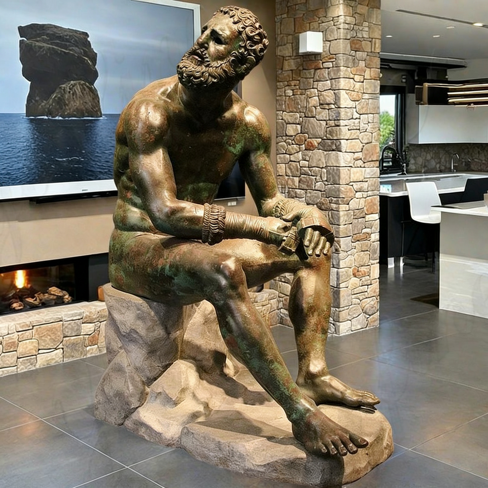 Bronze statue of a bearded man sitting on a rock in a modern interior setting.