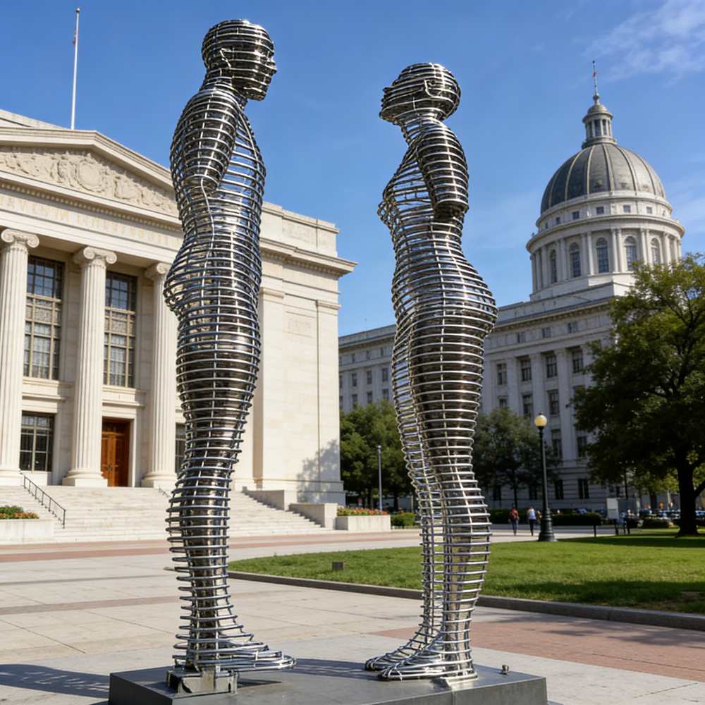 Metallic sculptures of two human figures in front of a large building with a dome.