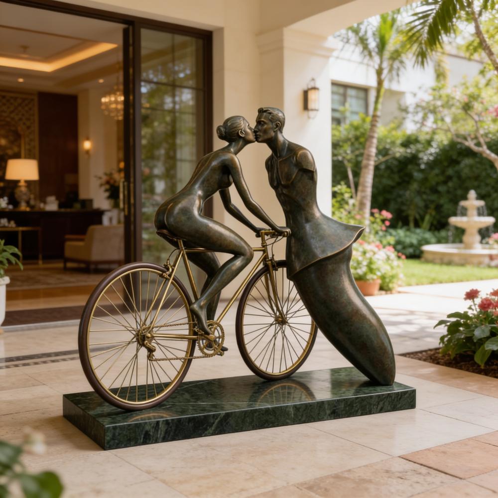 Bronze sculpture of a couple on a bicycle in an outdoor setting with a building and garden in the background.
Bronze artwork blending realism and abstraction in a romantic bicycle scene.