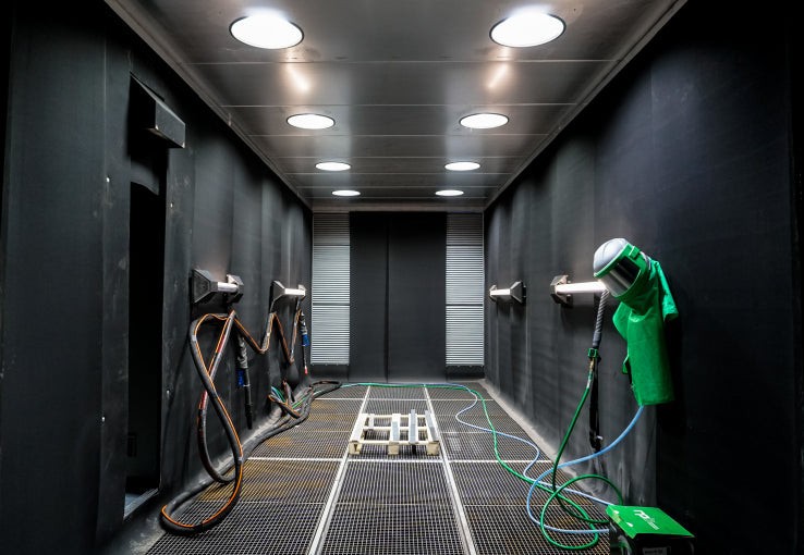 Industrial setting with black Powder Coating booth, green cleaning equipment, and a mesh floor.