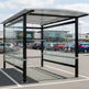 Side profile of modern shopping cart shelter featuring curved roof design and transparent glass enclosure.