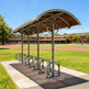 TAIMCO bike shelter installed in a park with curved roof and steel bike racks.