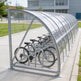 Bicycle shelter with multiple bicycles parked inside on a sidewalk.