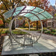Modern outdoor seating area with a curved glass canopy in a park setting.