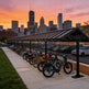 Bicycles parked under a shelter with a city skyline at sunset.
