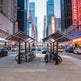 Bicycle racks on a city street with tall buildings and neon signs in the background