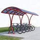 Red bicycle shelter with multiple bicycles parked underneath on a clear day.