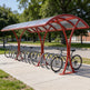 Red bicycle shelter with multiple bikes parked underneath in a park setting.