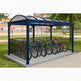 Blue bicycle shelter with multiple bicycles parked inside, set against a school building background.