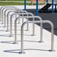 Row of metal bike racks on a concrete surface with grass and a bench in the background.