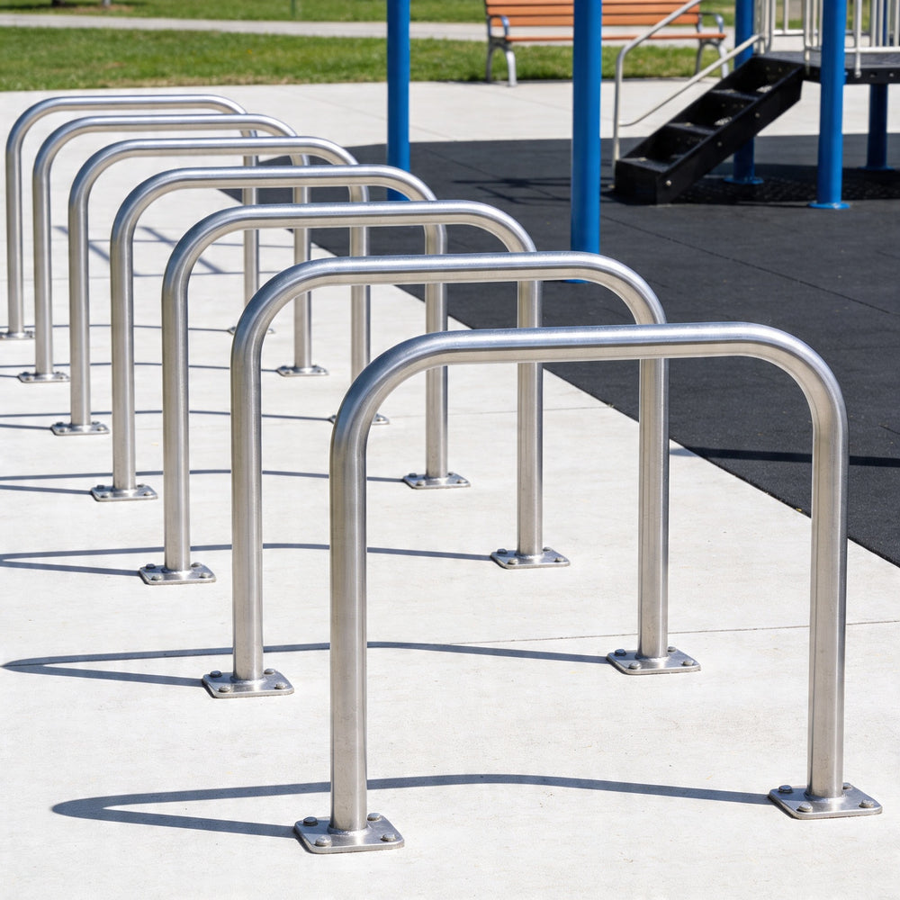 Row of metal bike racks on a concrete surface with grass and a bench in the background.
