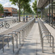 Bicycle racks along a sidewalk with people walking and biking in an urban setting.