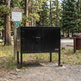 Black bearproof cabinet in a forest setting with a sign nearby.