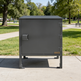 Gray metal cabinet with 'Taimco' branding on a sidewalk in a park setting