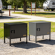 Two metal cabinets, one black and one gray, on a gravel surface with a campground background.