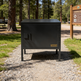 Black metal cabinet on a gravel path with trees and a wooden sign in the background