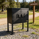 Black metal cabinet on a stand in a campground setting with trees and a 'Campground' sign in the background.