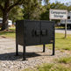 Black metal storage cabinet in a campground setting with a 'Campground Storage' sign in the background.
