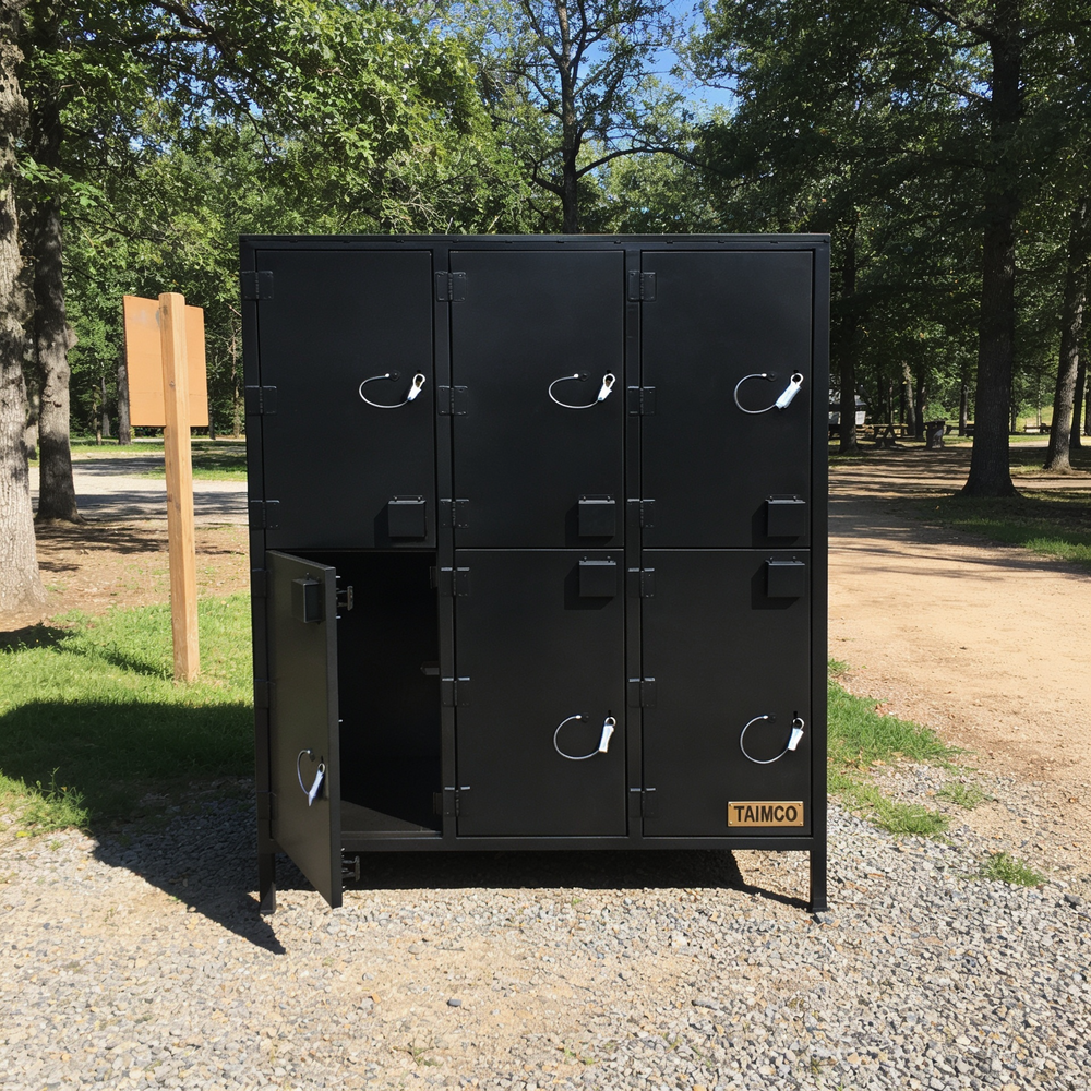 Black metal lockers with one door open, set against a natural background with trees and a path.