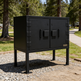 Black outdoor barbecue grill with 'TAMCO' branding in a park setting.