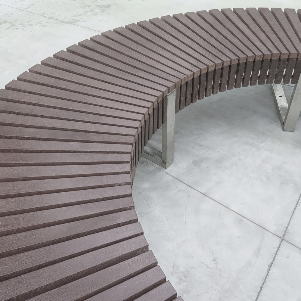 Curved outdoor bench with dark brown composite slats and stainless steel support posts on a light gray concrete surface.