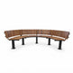 A curved outdoor bench with medium brown wooden slatted backrests and seat, supported by black metal posts, shown on a plain white background.
