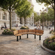 A curved wooden park bench with black metal legs situated in a paved public square with trees, street lamps, people sitting, and historic stone buildings in the background.