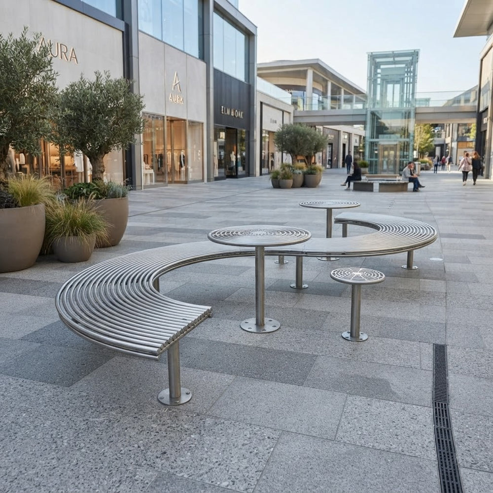 Curved stainless steel outdoor seating with integrated round tables in a modern shopping plaza.