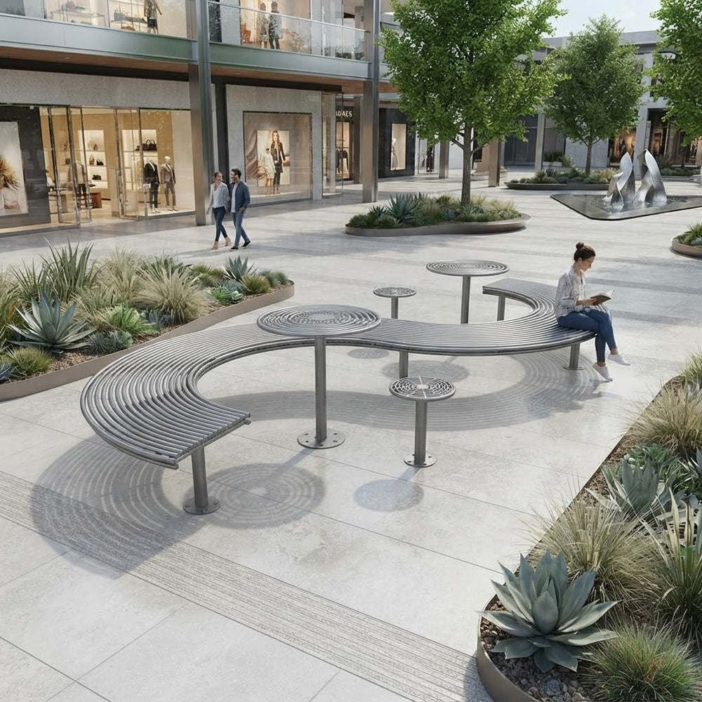Curved modern metal outdoor seating with integrated tables in a landscaped plaza, with a woman sitting on one bench reading and shoppers walking in the background.